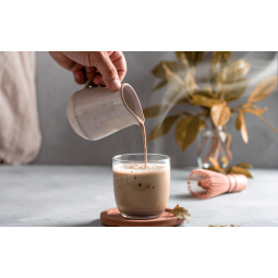 Foto con mano che versa Chai da un bricco dentro ad un bicchiere appoggiato su un tavolo